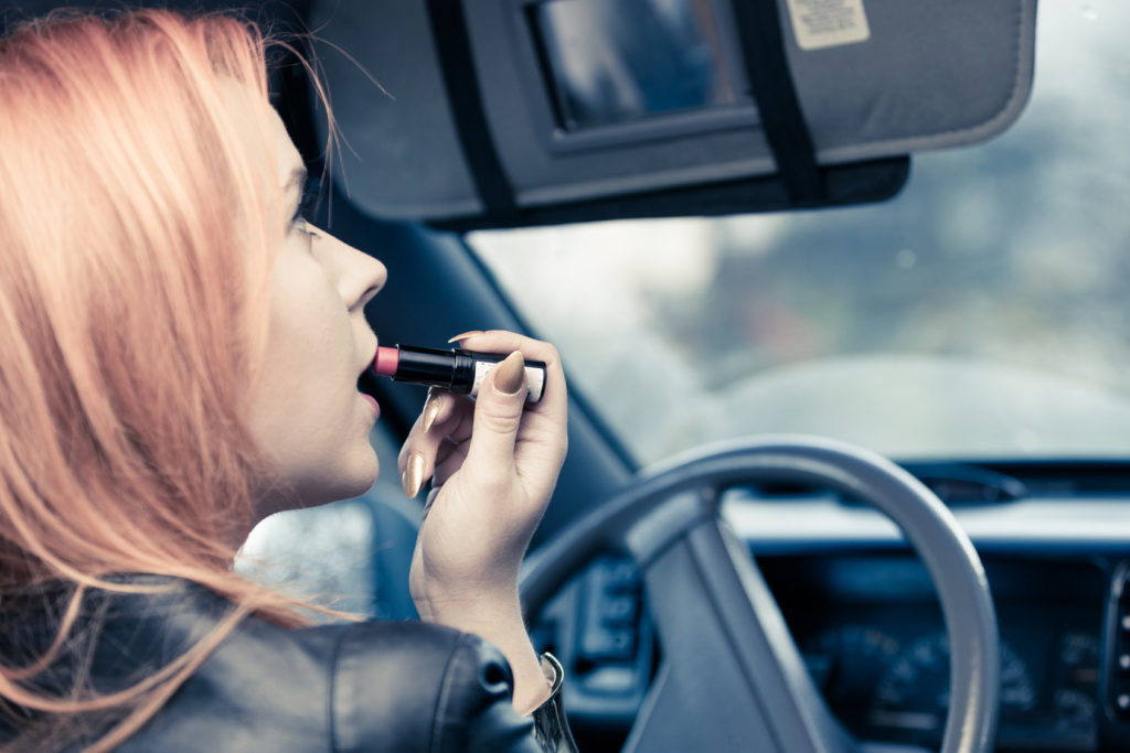 woman applying lipstick inside of her car
