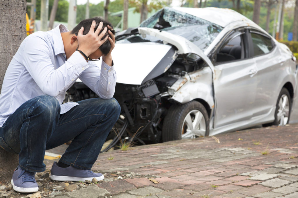 frustrated man sitting near crashed car