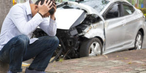 frustrated man sitting near crashed car