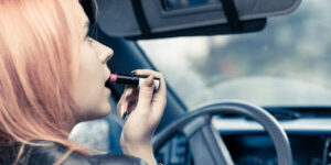 woman applying lipstick inside of her car